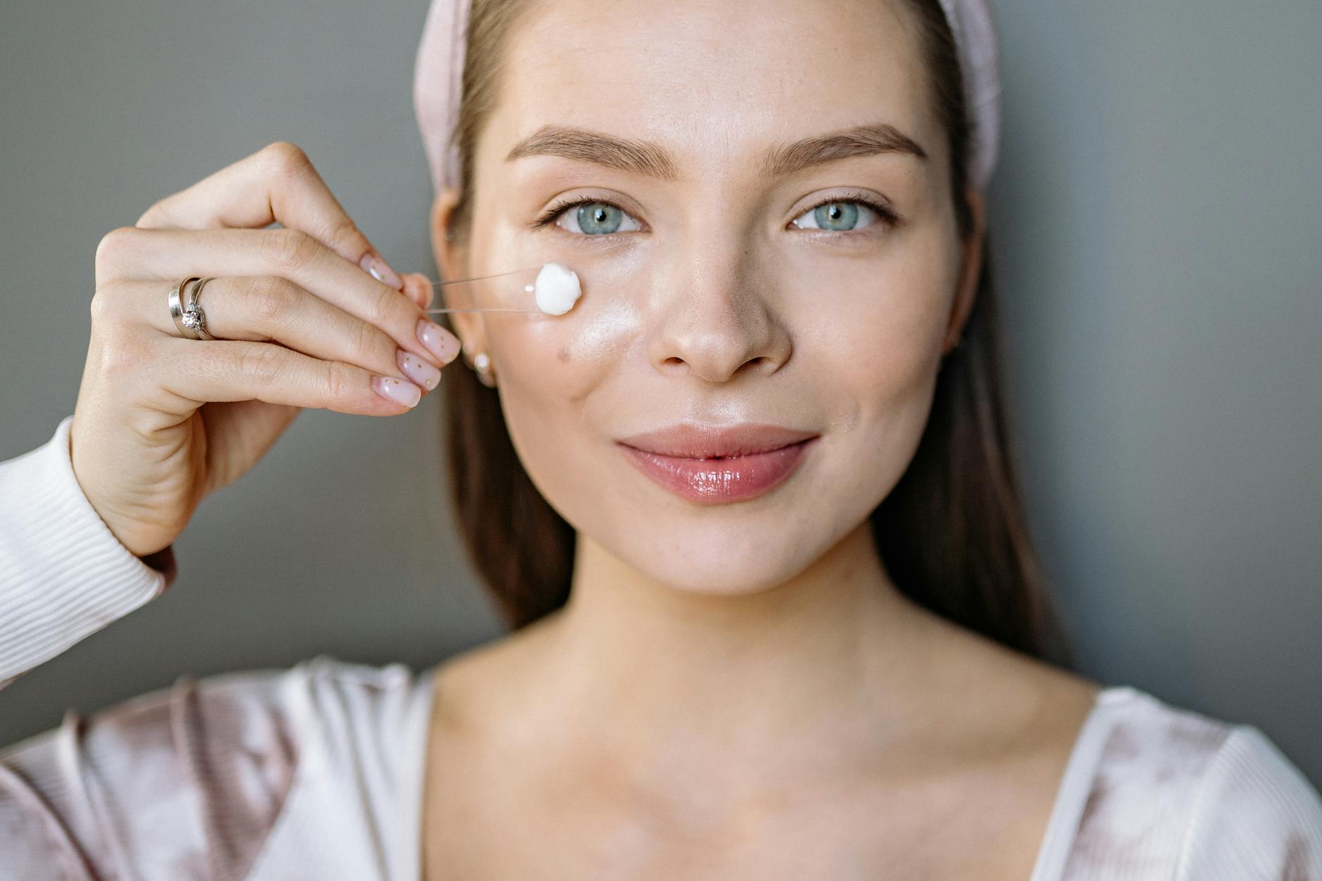Smiling woman applying facial cream for skincare routine - spring skincare tips
