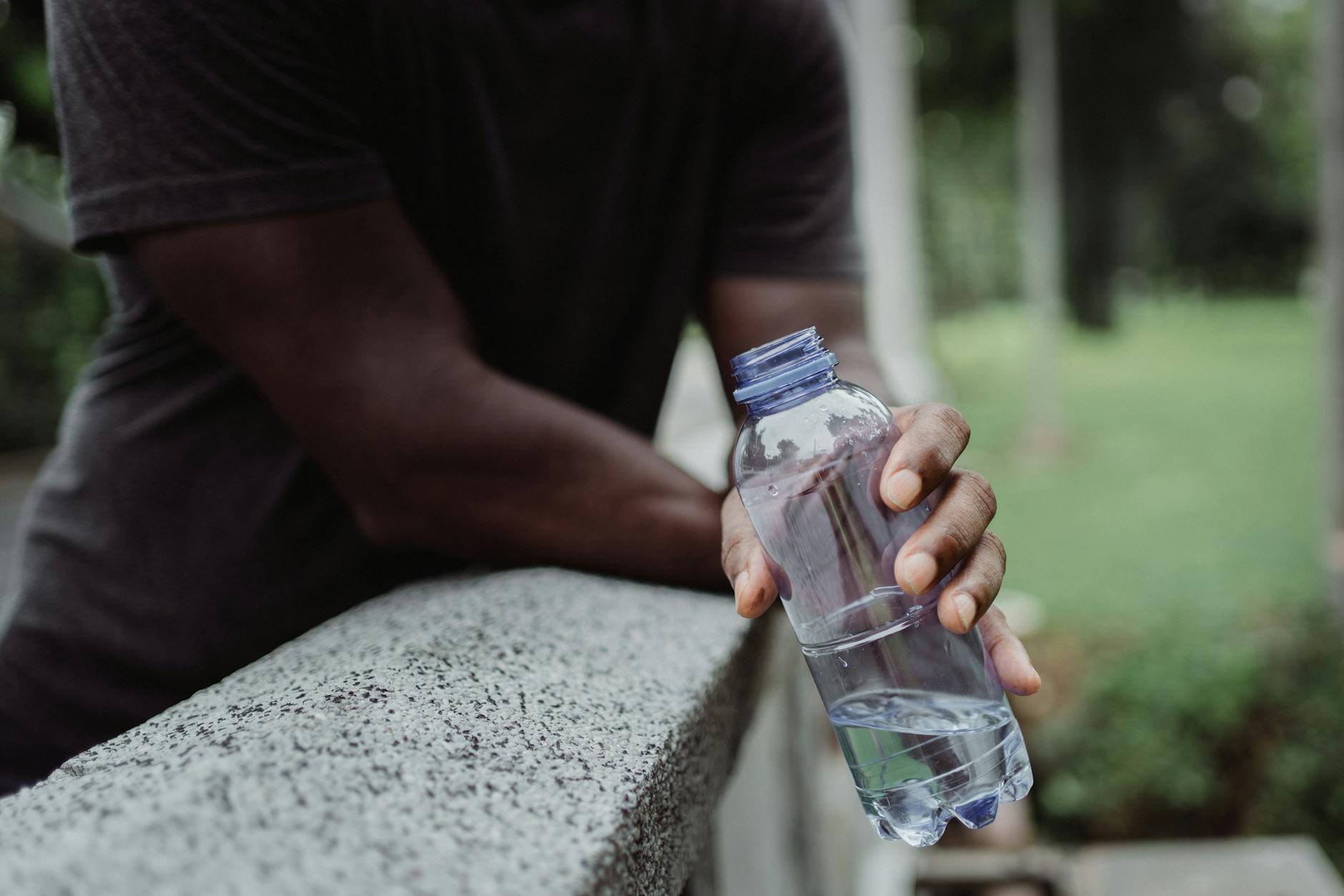 A person holds a plastic water bottle on a concrete rail outdoors, emphasizing hydration. - spring sports hydration