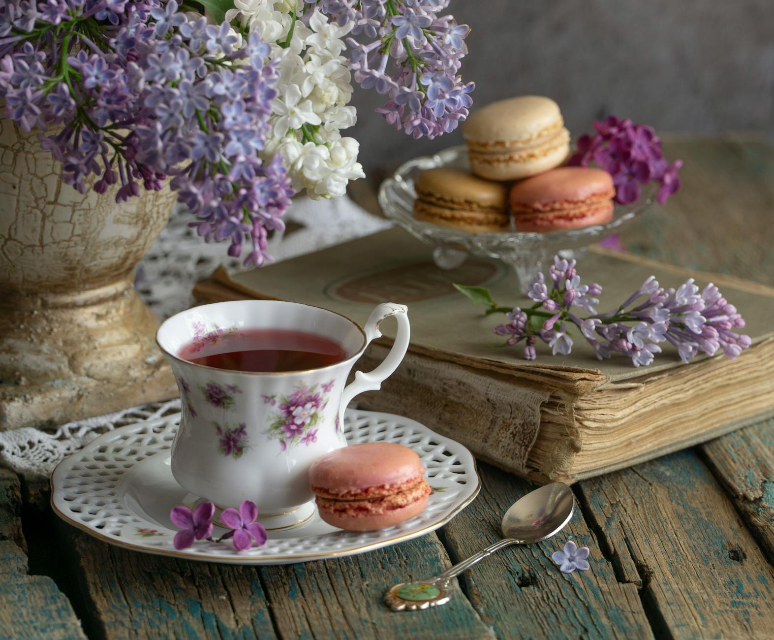 Charming tea setup with lilac flowers, macarons, and vintage elements in soft lighting. - spring sweet cravings