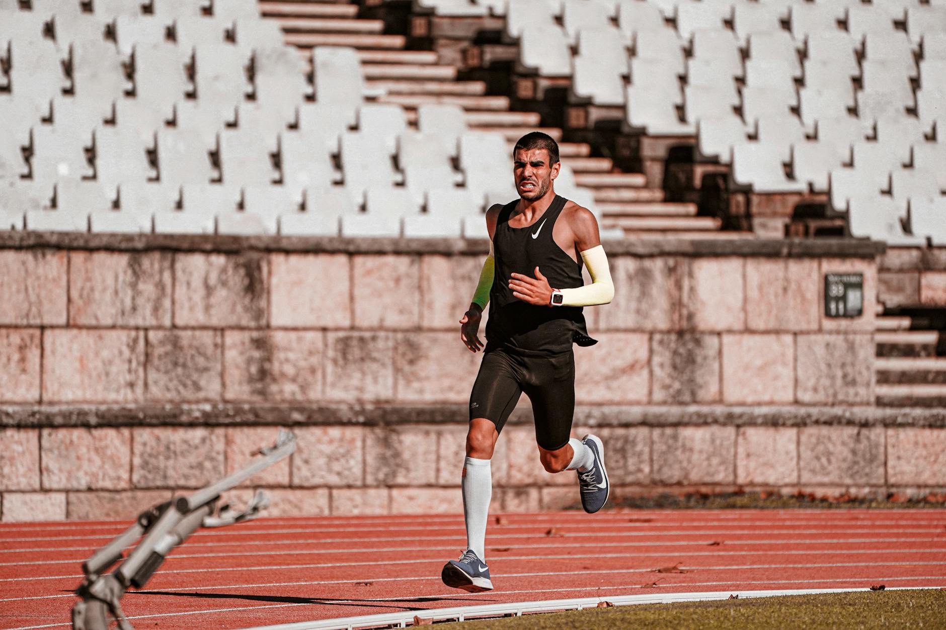 A determined male athlete runs on a track in a sunny stadium, showcasing endurance and speed. - strength training runners