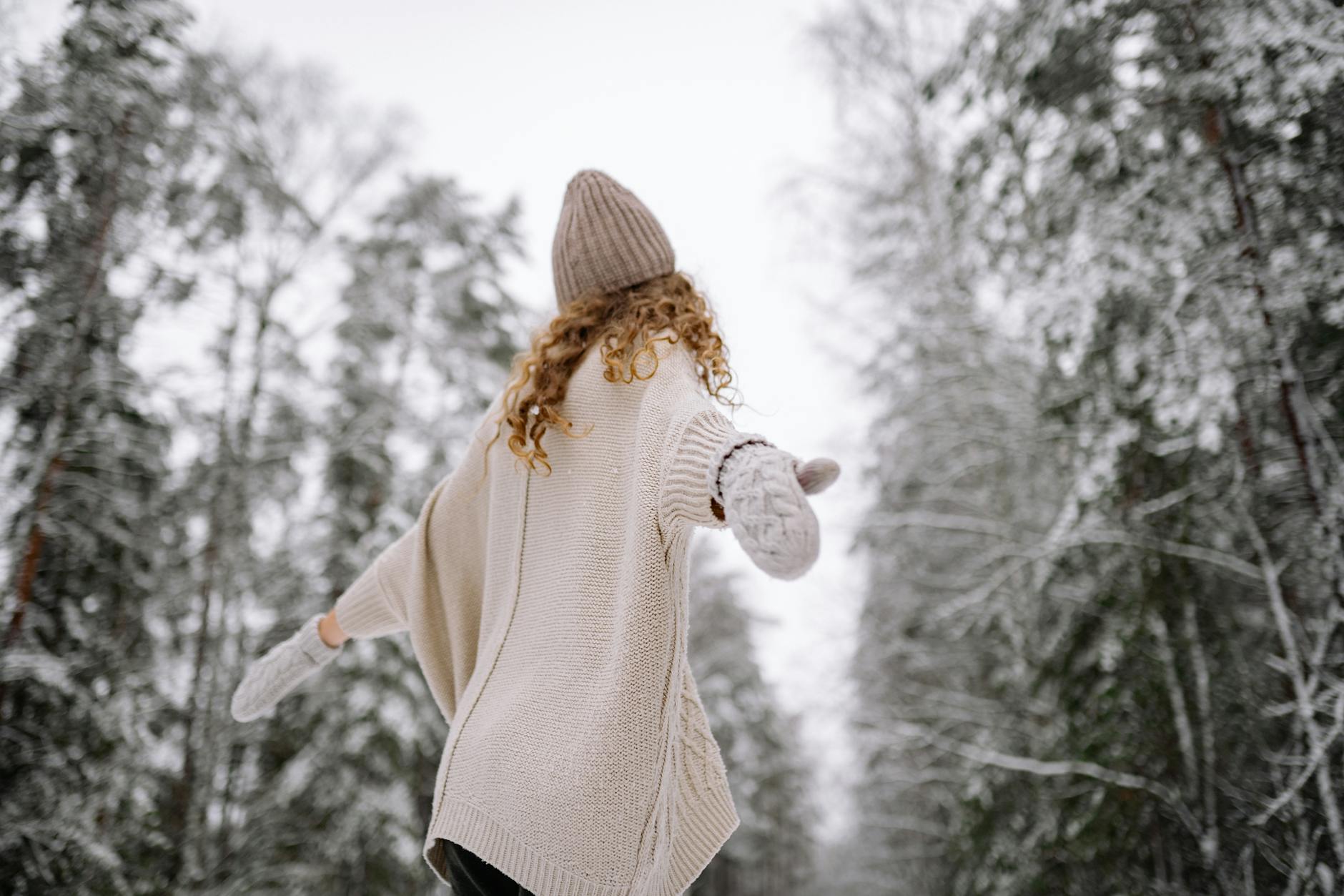 Woman in knitwear enjoying snowy forest scene in winter. Back view with arms outstretched. - winter body reset