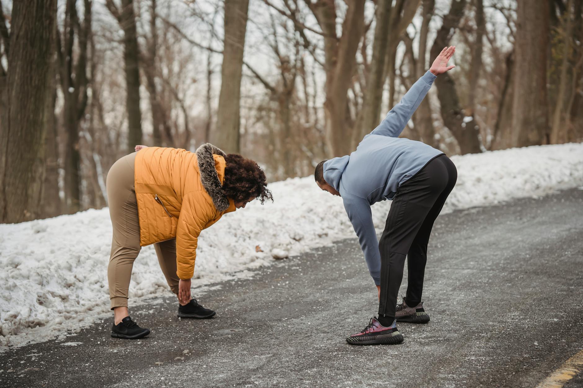 Full body side view of anonymous African American couple in sportswear doing warm up exercises on asphalt walkway in winter time - winter body reset